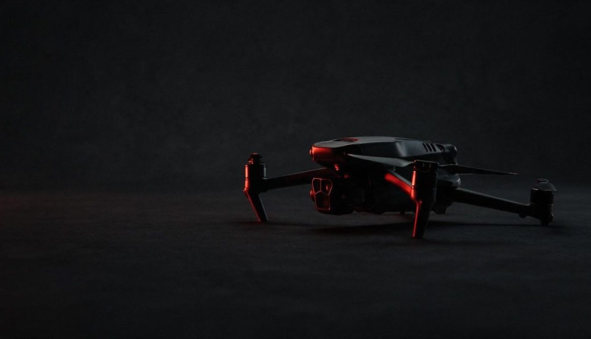 A folded quadcopter drone on a dark studio background, a red rim light tracing its edge
