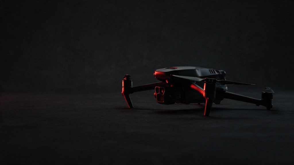 A folded quadcopter drone on a dark studio background, a red rim light tracing its edge